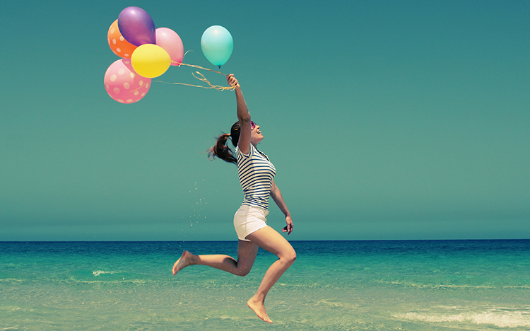 Teaser Grusskarten: Frau mit Liuftballons hüpft am Strand